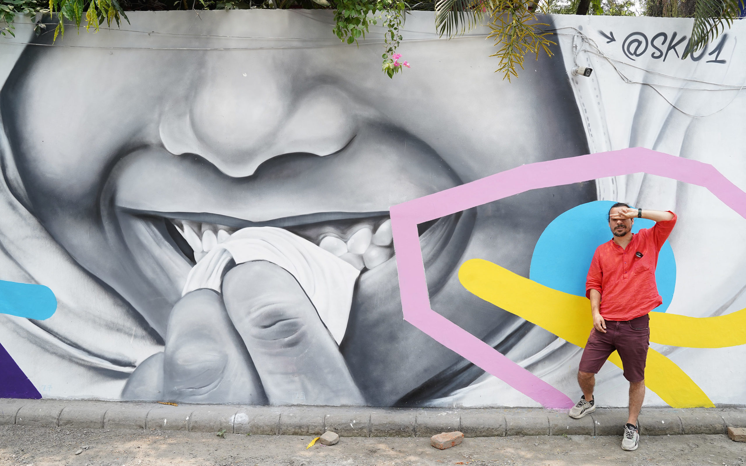 Artiste skio posant devant une de ses fresque murale colorées dans la ville